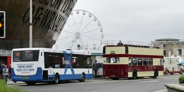 Modern and heritage buses at the Cardiff Bay terminus in front of the Wales Millennium Centre, with the bay's big wheel behind