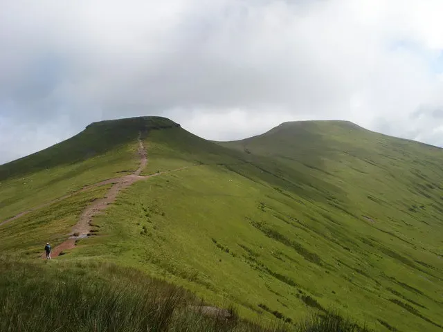 Corn Du and Pen y Fan seen along the grassy ridge, with the worn main path climbing towards the flat summits